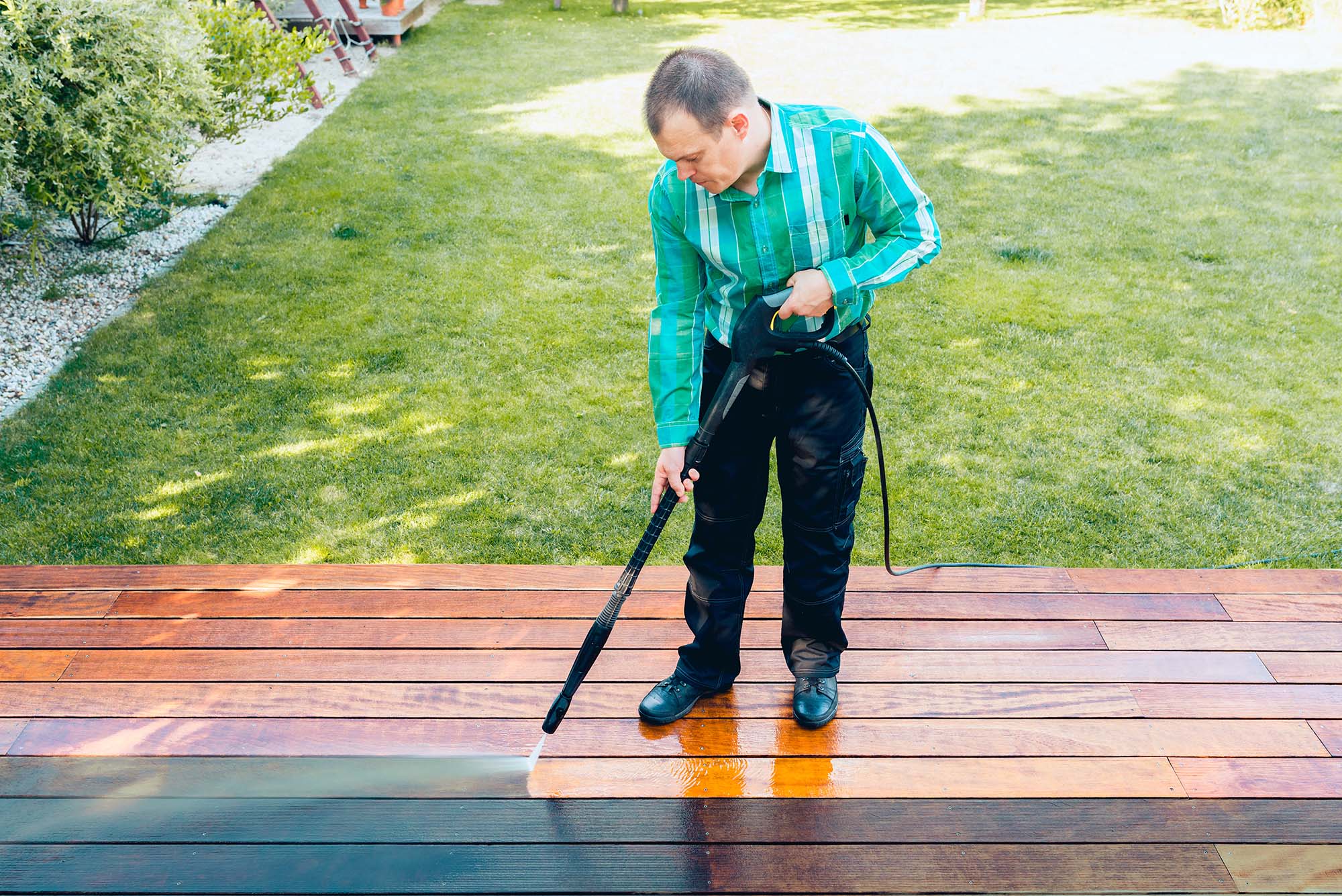 Man in a backyard cleaning a timber deck with a high pressure cleaner